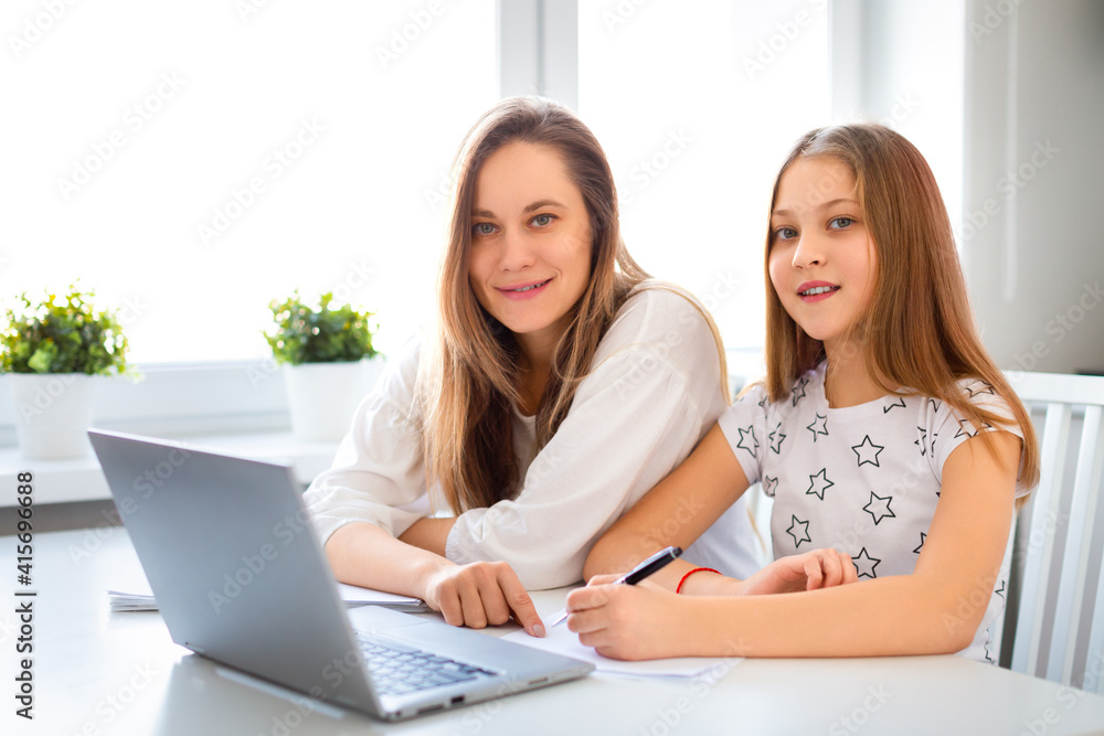 Mom helps her daughter do her homework online. They looking at camera.