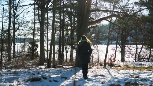 Young woman walking toward the frozen sea between the pine trees photo