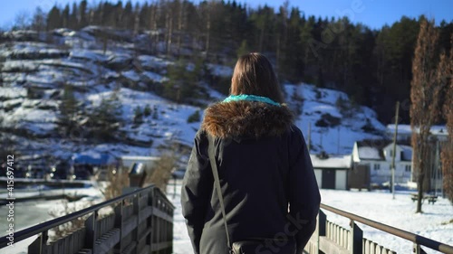 Young woman walking over a bridge in a snowy forest landscape by the frozen sea photo