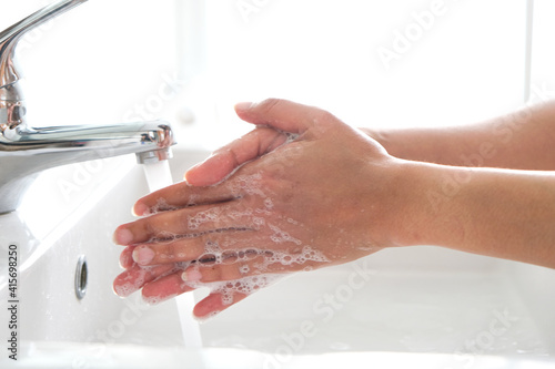 Hands of woman wash their hands in a sink with foam to wash the skin and water flows through the hands. Concept of health, cleaning and preventing germs and coronavirus from contacting hands
