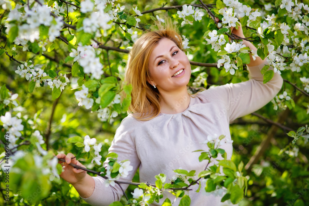 Portrait of a fat plump young woman with red hair and a blooming apple tree on a white floral background in a park on a spring day. Happy plus-size girl. Portrait of a fat plump young woman with red hair and a blooming apple tree on a white floral background in a park on a spring day. Happy plus-size girl.