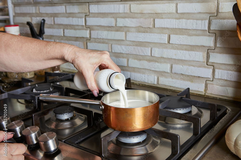 Cooking at home in the kitchen using a recipe from the Internet. woman pours cream into a saucepan on the gas stove Cooking at home in the kitchen using a recipe from the Internet. woman pours cream into a saucepan on the gas stove