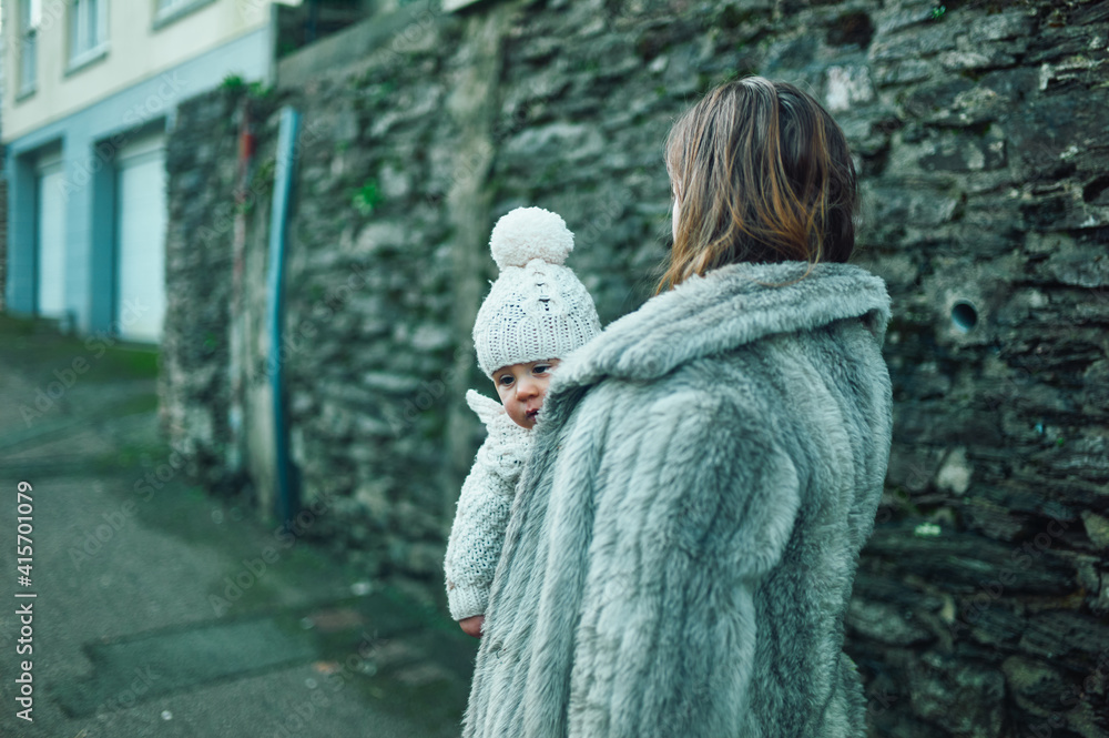 Young mother walking in the street with baby in sling in winter