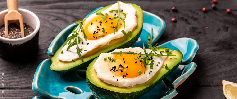 Fototapeta premium Avocado baked with eggs, fresh parsley on black background, banner, menu recipe place for text, top view