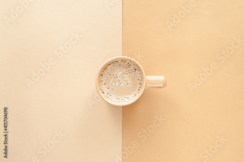 Hot cappuccino with milk foam in a beige cup on a beige background. View from above, Place for text. Monochrome and minimalism.