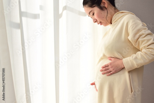 A pregnant woman in her twenties is holding her hand on her enlarged belly.