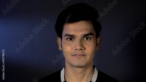 Portrait of young handsome Indian man cheerfully looking straight at the camera. Closeup shot of a clean shaven youngster standing confidently against a black background - people and lifestyle concept