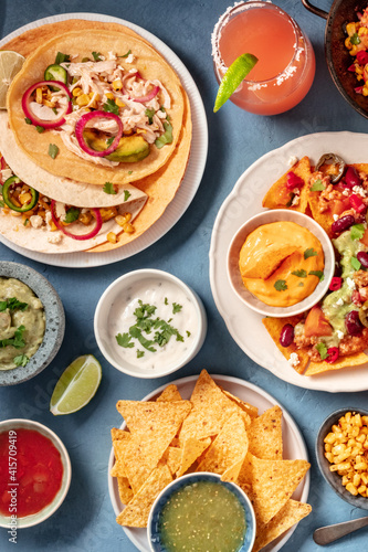Mexican food on a blue background. Nachos, tacos and dips, cocktails, overhead shot