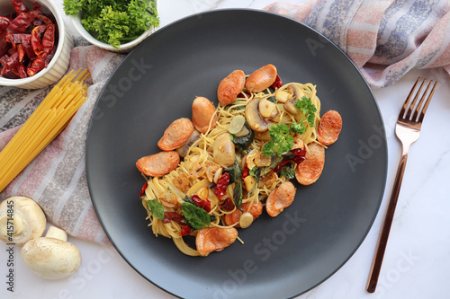 Capellini with Sausage, garlic, champingon mushroom, basil and dry chili - Italian food sometimes called angel hair pasta in black plate of marble table photo