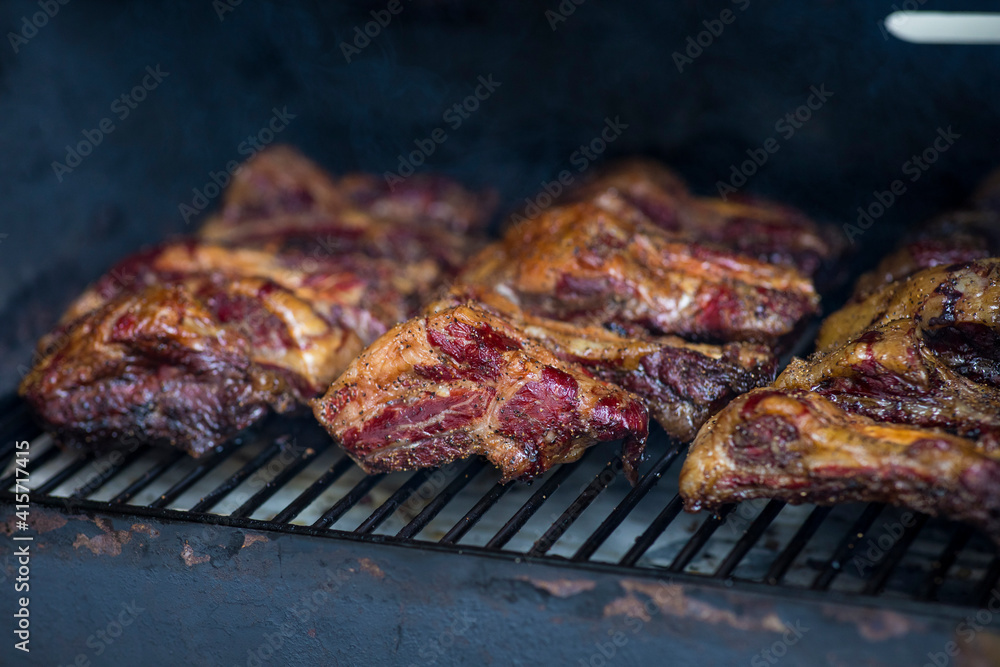 Smoke rising around a slow cooked beef brisket on the grill grates of a smoker barbecue. Grilled spare ribs macro - pork ribs