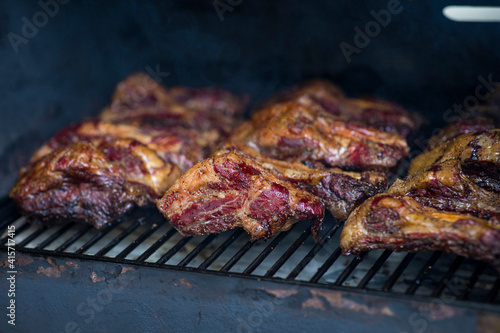 Smoke rising around a slow cooked beef brisket on the grill grates of a smoker barbecue. Grilled spare ribs macro - pork ribs