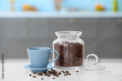 Cup and jar with coffee beans on table in modern kitchen