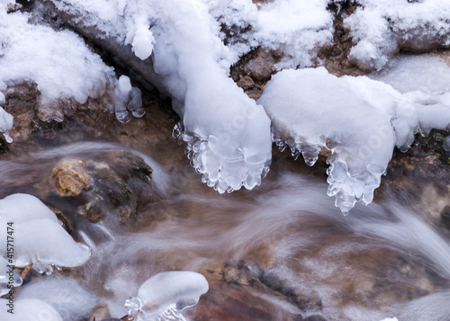 frozen fast flowing spring water, icy rocks and water stream, frosty tree roots, beautiful ice and water texture © ANDA