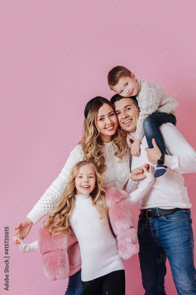 Family portrait. Happily posing together. Parents and their young children. Boy sitting on fathers shoulders. Girl holding mother's hands. Bright top, dark bottom. Over dark pink. Family portrait. Happily posing together. Parents and their young children. Boy sitting on fathers shoulders. Girl holding mother's hands. Bright top, dark bottom. Over dark pink.
