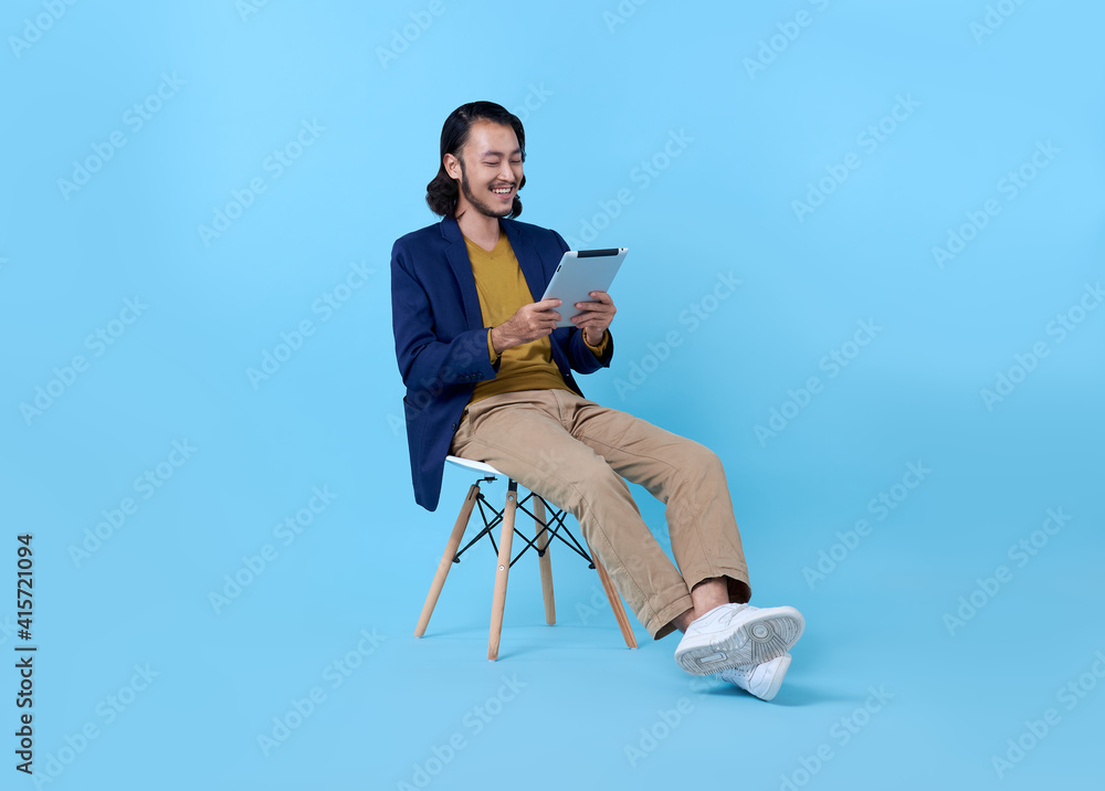 Business man asian happy smiling using a digital tablet while sitting on chair isolated on bright blue background.