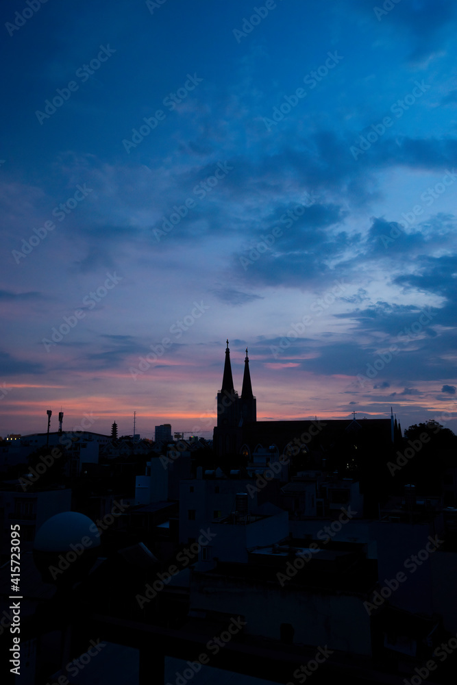 Fototapeta premium Beautiful red and blue sunrise sky with clouds over black silhouette of city with tower of church on horizon. Silhouette of the catholic church and cross