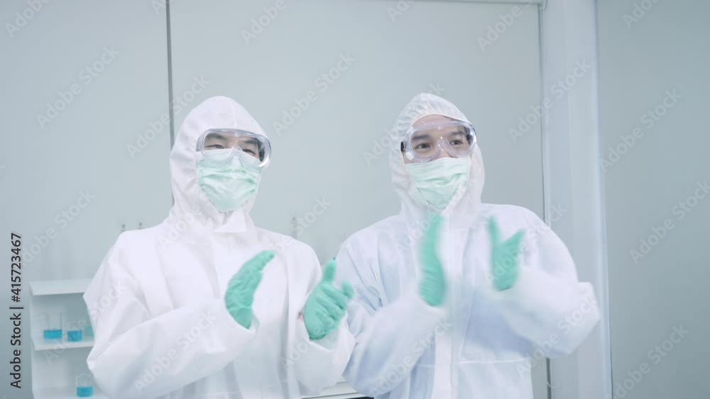 Two asian man scientist is wearing Personal Protective Equipment (PPE) while celebrating success with Holding Hands and applause, clapping in laboratory. Medical successful concept. Slow motion Two asian man scientist is wearing Personal Protective Equipment (PPE) while celebrating success with Holding Hands and applause, clapping in laboratory. Medical successful concept. Slow motion