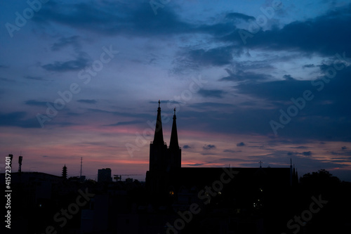 Beautiful red and blue sunrise sky with clouds over black silhouette of city with tower of church on horizon. Silhouette of the catholic church and cross