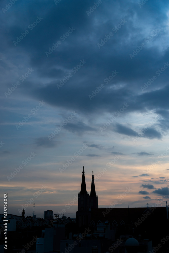 Beautiful red and blue sunrise sky with clouds over black silhouette of city with tower of church on horizon. Silhouette of the catholic church and cross