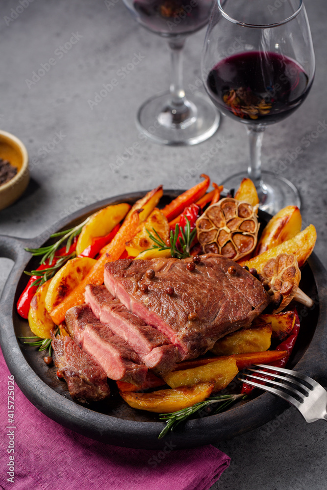 Steak with baked vegetables and red wine glases. Vertical image, grey background, copy space. Steak with baked vegetables and red wine glases. Vertical image, grey background, copy space.