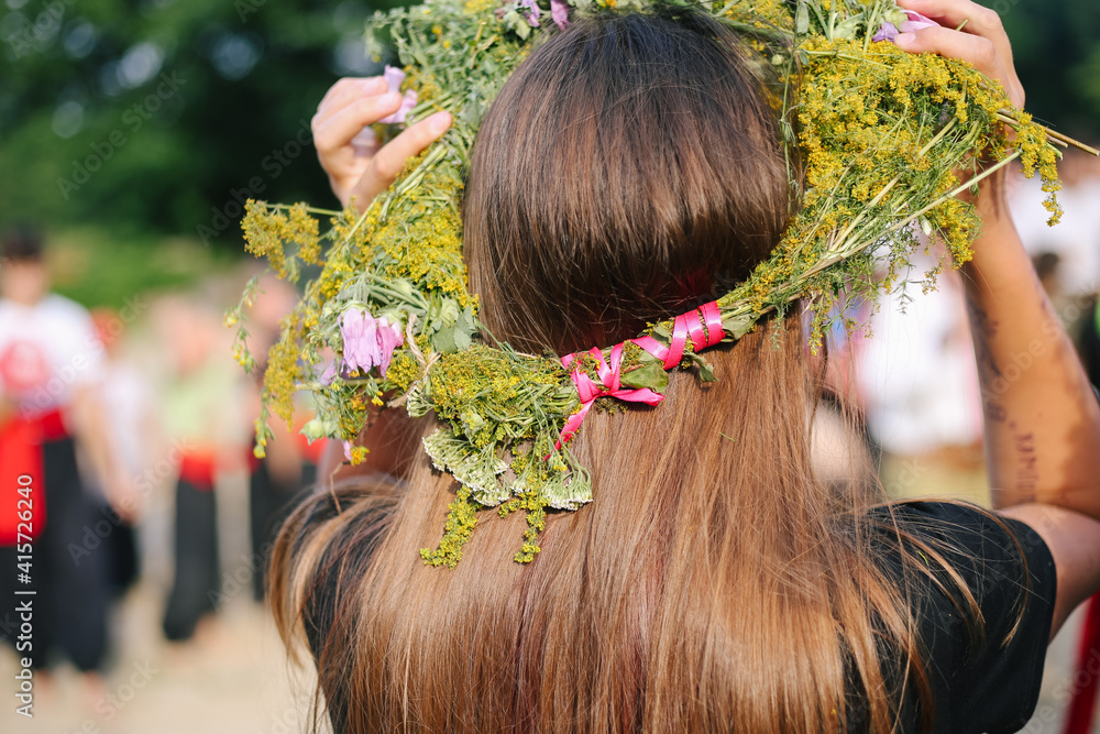 Naklejka premium Girl from the back in a wreath of flowers, wildflowers at the celebration of a traditional Slavic holiday Ivana Kupala