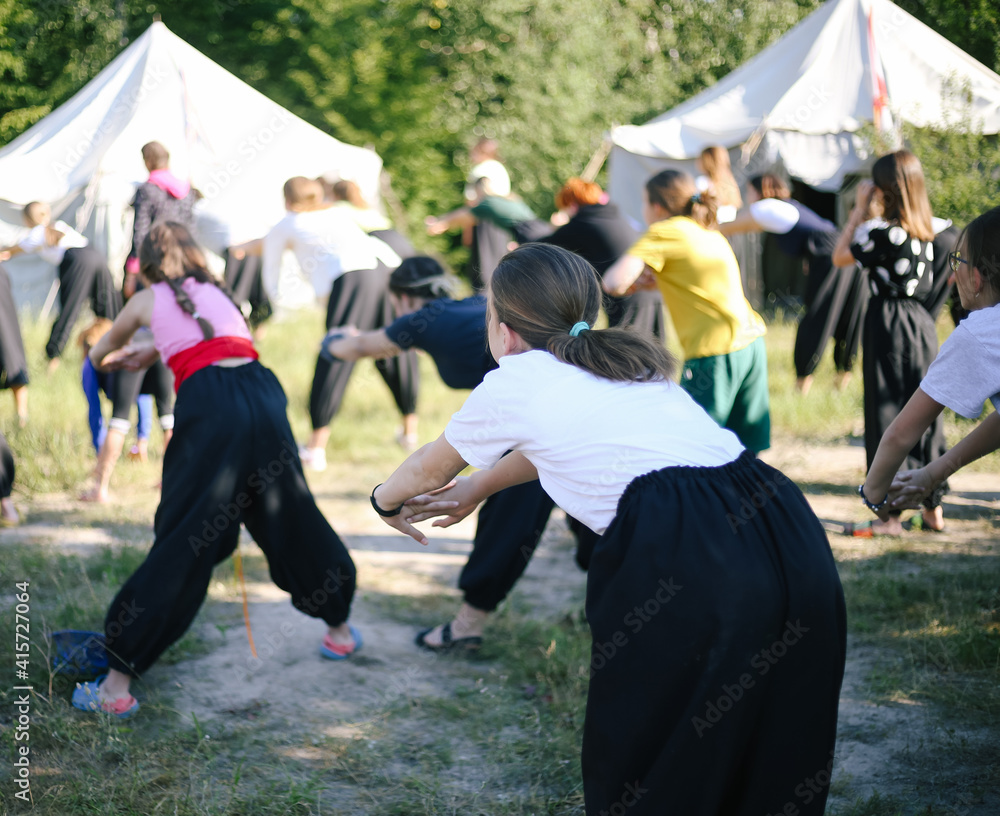 Obraz premium Girls from the back stretch up. Exercises for warming up. Group of children doing morning sports in summer camp