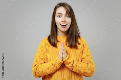 Young pretty attractive nice cute pleaded woman 20s wearing casual knitted yellow sweater hands folded in prayer gesture, begging about something isolated on grey color background studio portrait.