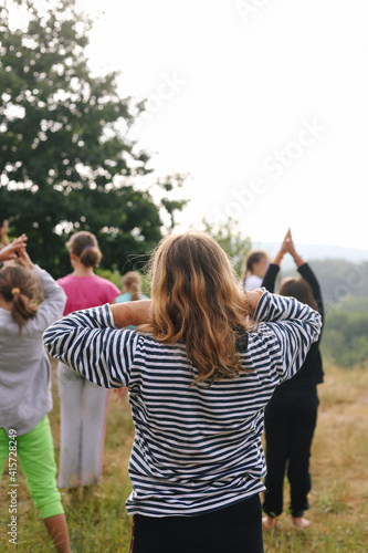 Girl kneads the neck. Group of children doing morning exercises yoga-sport outdoors in nature in a summer camp