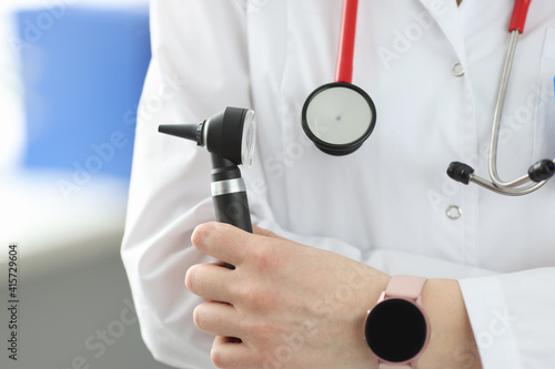 Otorhinolaryngologist holding otoscope in his hands in clinic closeup photo