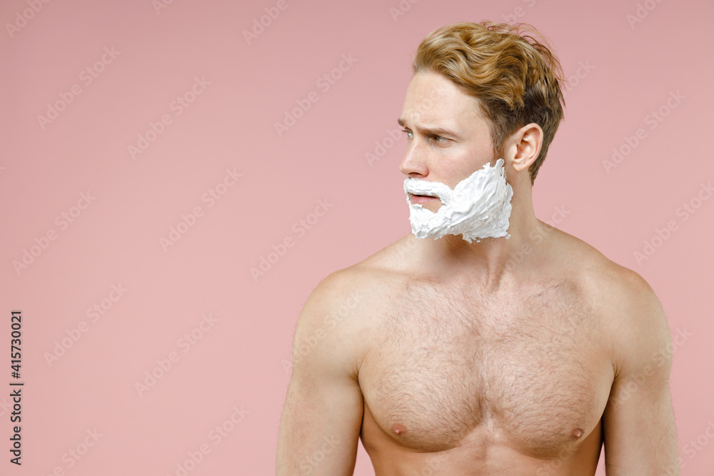 Handsome bearded naked young man 20s years old perfect skin face covered with shaving foam looking aside isolated on pink background studio portrait. Skin care healthcare cosmetic procedures concept.