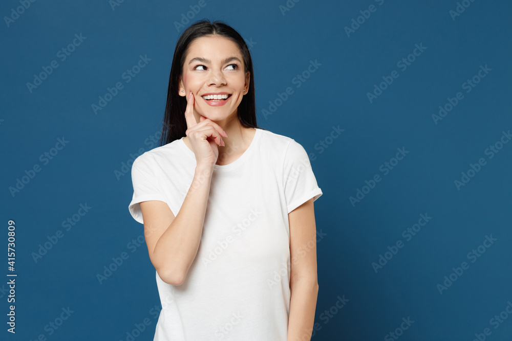 Young smiling pretty dreamful pensive wistful positive attractive beautiful latin woman 20s wearing white casual basic t-shirt prop up chin look aside isolated on dark blue background studio portrait. Young smiling pretty dreamful pensive wistful positive attractive beautiful latin woman 20s wearing white casual basic t-shirt prop up chin look aside isolated on dark blue background studio portrait.