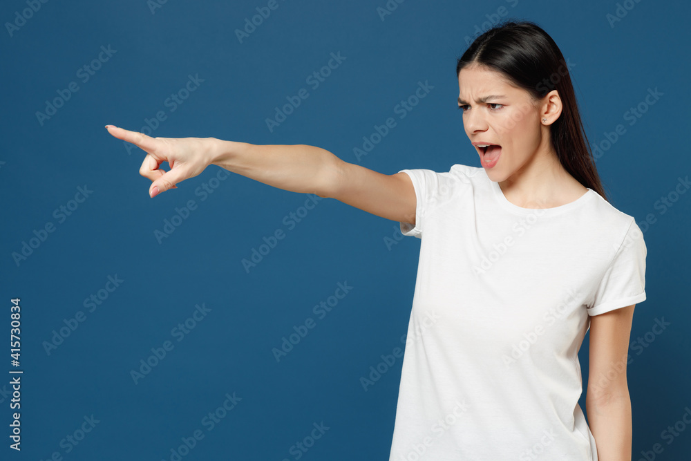 Young strict indignant angry latin woman 20s wearing white casual basic t-shirt point index forefinger finger aside scream shout command do it isolated on dark blue color background studio portrait. Young strict indignant angry latin woman 20s wearing white casual basic t-shirt point index forefinger finger aside scream shout command do it isolated on dark blue color background studio portrait.