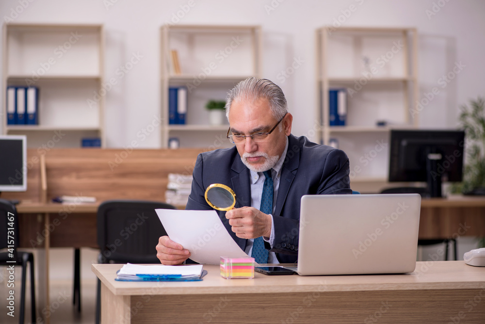 Old male employee auditor holding loupe at workplace Old male employee auditor holding loupe at workplace