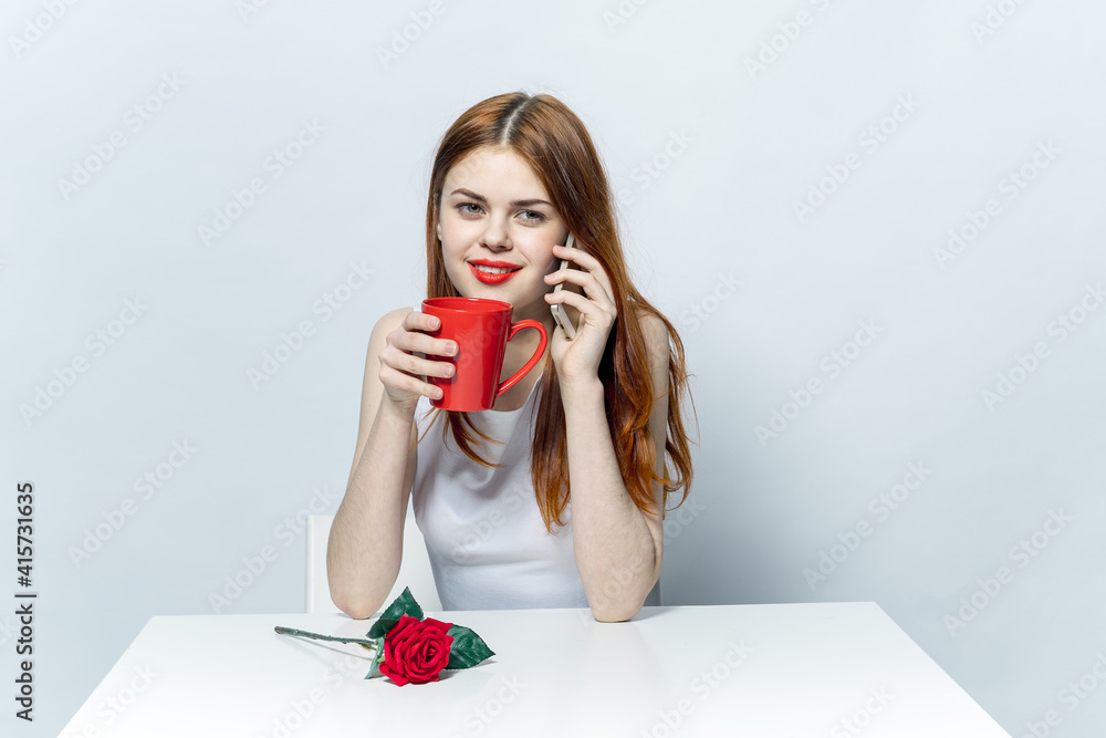 elegant woman sitting at the table drinking from a red mug and talking on the phone elegant woman sitting at the table drinking from a red mug and talking on the phone
