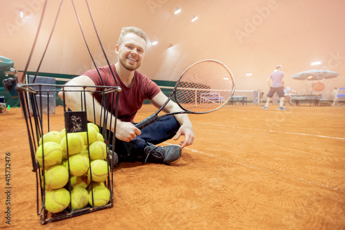 Smiling man tennis trainer player with racket and ball on court © Parilov