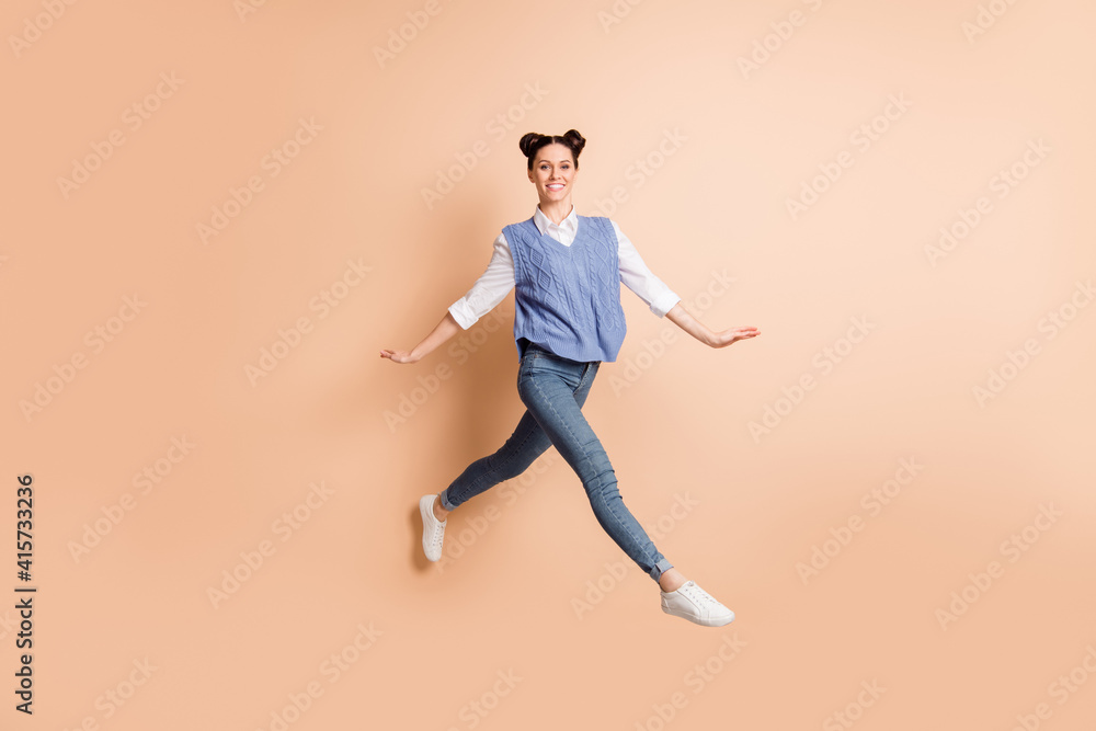 Full size profile photo of brunette optimistic lady jump go wear white shirt blue vest jeans sneakers isolated on beige color background