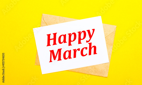 On a yellow background, an envelope and a card with the text HAPPY MARCH. View from above