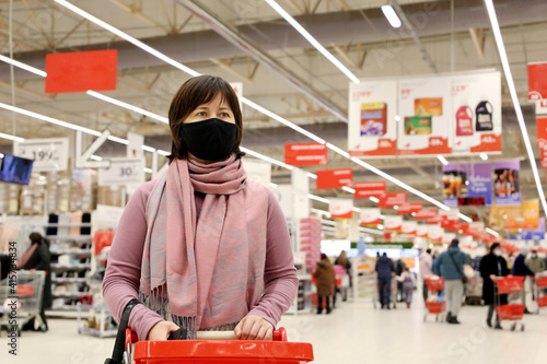 фотографія Woman in medical mask walking with a shopping cart in a mall on people background