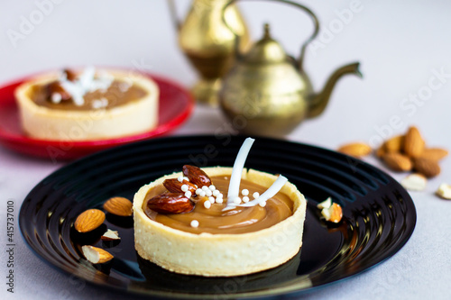 nougat or caramel filling tartlets with nuts, sweet dessert with whole almonds on black plate, french confectionery