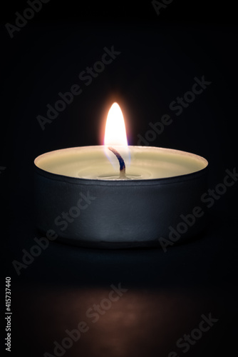 A burning candle on a dark background with a flare in the foreground.