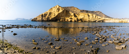 panorama view of a secluded cove and beach on the Meiterranean coast of Spain with caves and sandstone cliffs behind photo