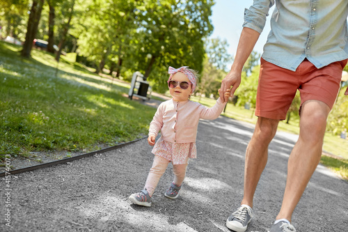 family, fatherhood and people concept - father with baby daughter walking at summer park