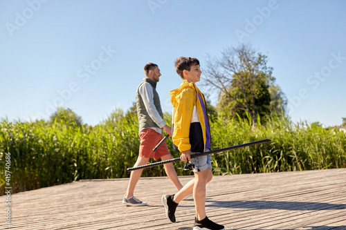family, generation, summer holidays and people concept - happy smiling father and son with fishing rods on river berth