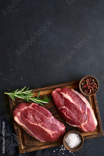 Raw organic marbled beef steaks with spices on a wooden cutting board . Top view with copy space.