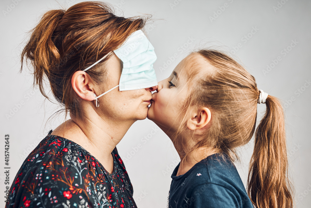 Little girl moving her mom's face mask on eyes and giving a kiss her mother. Funny moments during quarantine and covid-19 pandemic Little girl moving her mom's face mask on eyes and giving a kiss her mother. Funny moments during quarantine and covid-19 pandemic