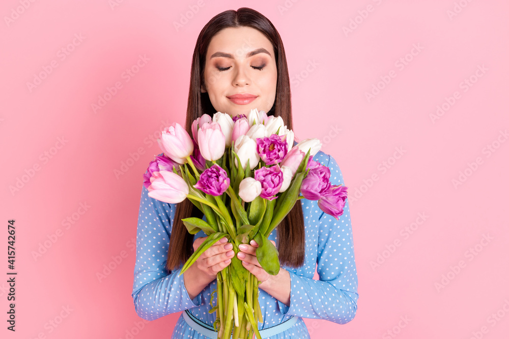 Photo of young charming sweet smiling lovely dreamy girl in dotted blouse smell flowers isolated on pink color background