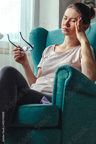 Canvastavla Young woman with glasses in hands sits in a chair and suffers from headache