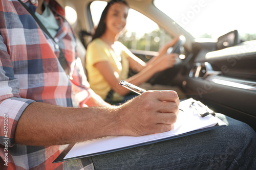 Instructor with clipboard writing result of exam in car, closeup. Driving school