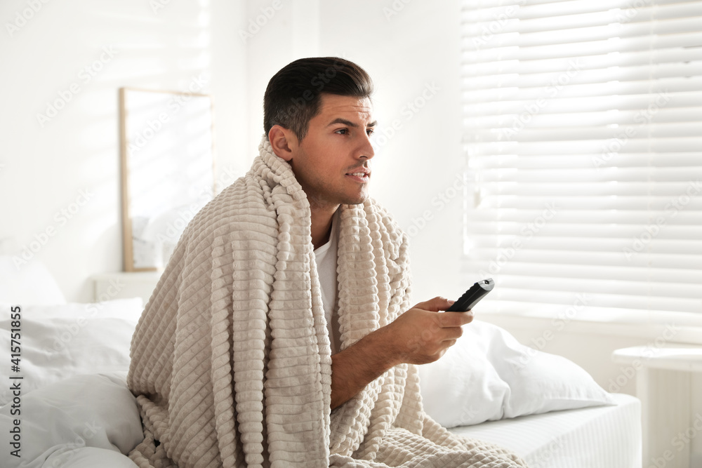 Man covered with warm beige plaid watching television in bedroom Man covered with warm beige plaid watching television in bedroom
