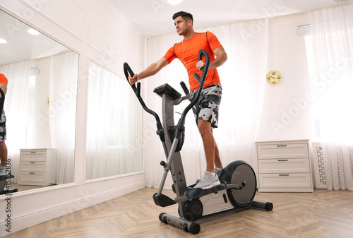 Man using modern elliptical machine at home photo